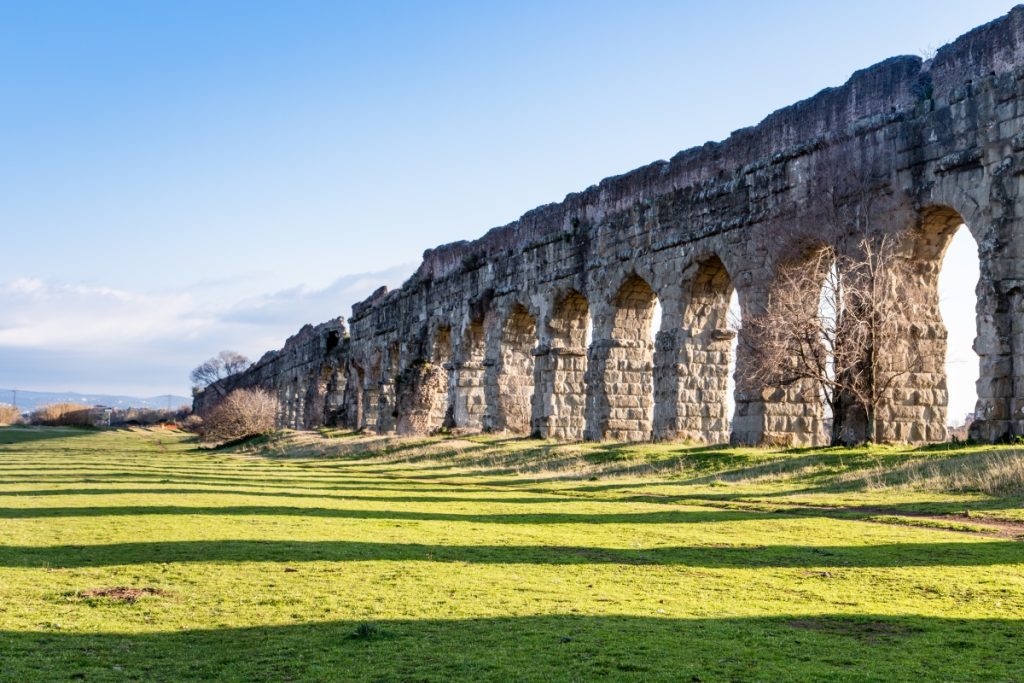 Ancient Roman arches of Acquedotto Claudio stretching across a green landscape near Rome, a true Lazio best-kept secret.