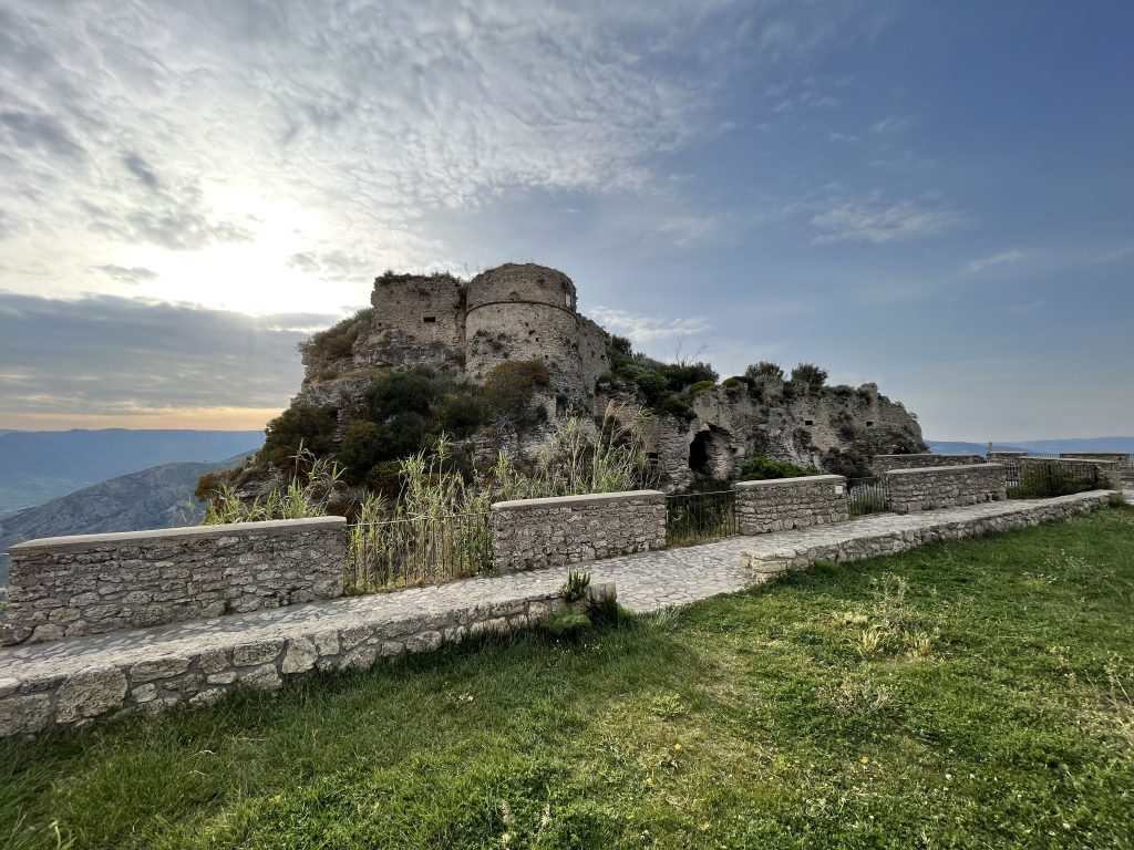 Panoramic view of Gerace Castle perched on a hilltop, surrounded by historic buildings and olive groves.