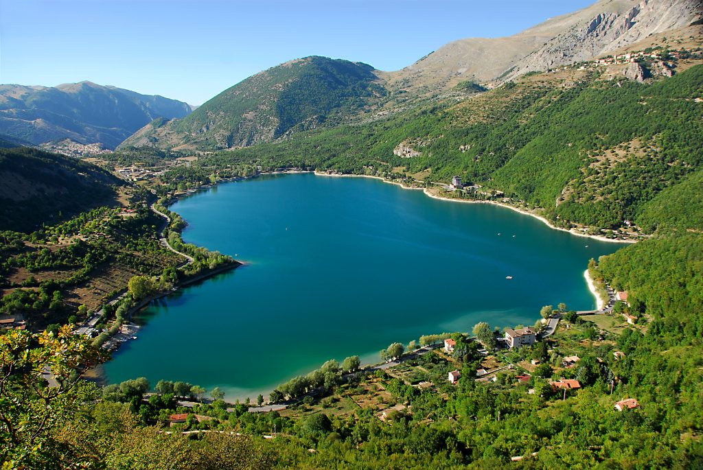 Travel to Abruzzo for a scenic view of Lago di Scanno surrounded by forested hills and reflecting the clear sky above.