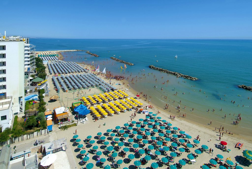 Wide sandy beach along Lungomare di Montesilvano with calm waves and colorful umbrellas under a clear sky.