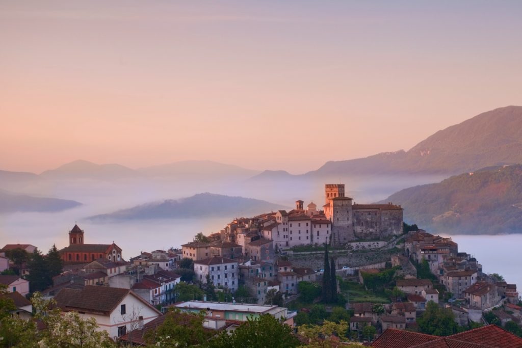 Historic stone buildings of Roviano village nestled on a rocky hillside surrounded by lush green valleys