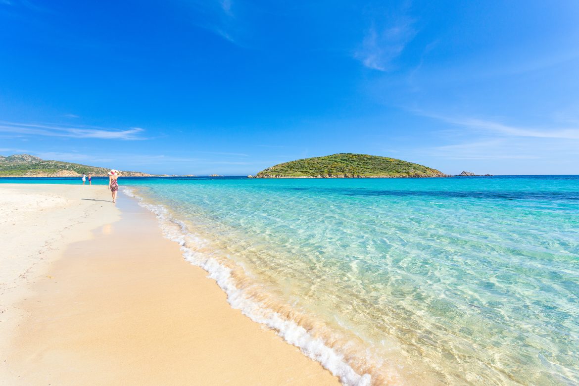 Travel Sardinia and experience crystal-clear waters and soft white sand at Spiaggia di Tuerredda, framed by green hills and calm Mediterranean waves.