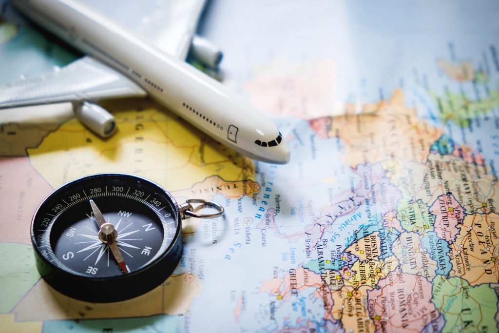 Compass on a world map next to a small plate, symbolizing navigation and planning in travel safety tips for backpackers.